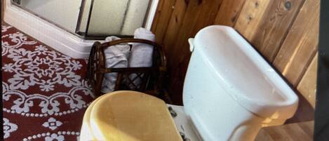 A bathroom with a wooden floor, a white toilet, a wooden chair, and a towel rack.