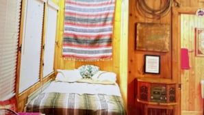 Habitación de cabaña de madera con una cama, estante con objetos y un adorno colgado en la pared.