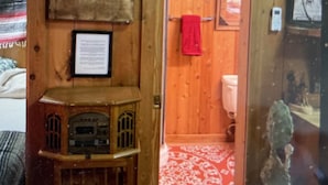 Interior de madera con una radio antigua, un tapete rojo estampado y una puerta con una toalla colgada.