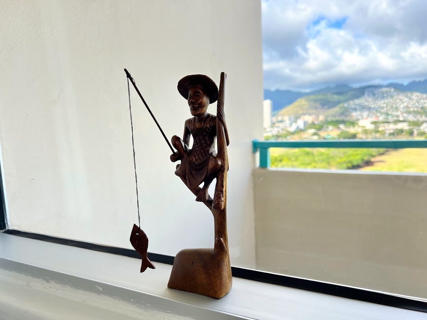 Una estatua de madera de un pescador en un alféizar con vistas al paisaje costero.