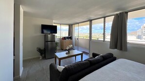 A hotel room with a bed, a TV, a small table with a plant, and a view of the city through large windows. - Penthouse in Waikiki with ocean & mountain views 5 minutes walk to Waikiki beach (Honolulu)