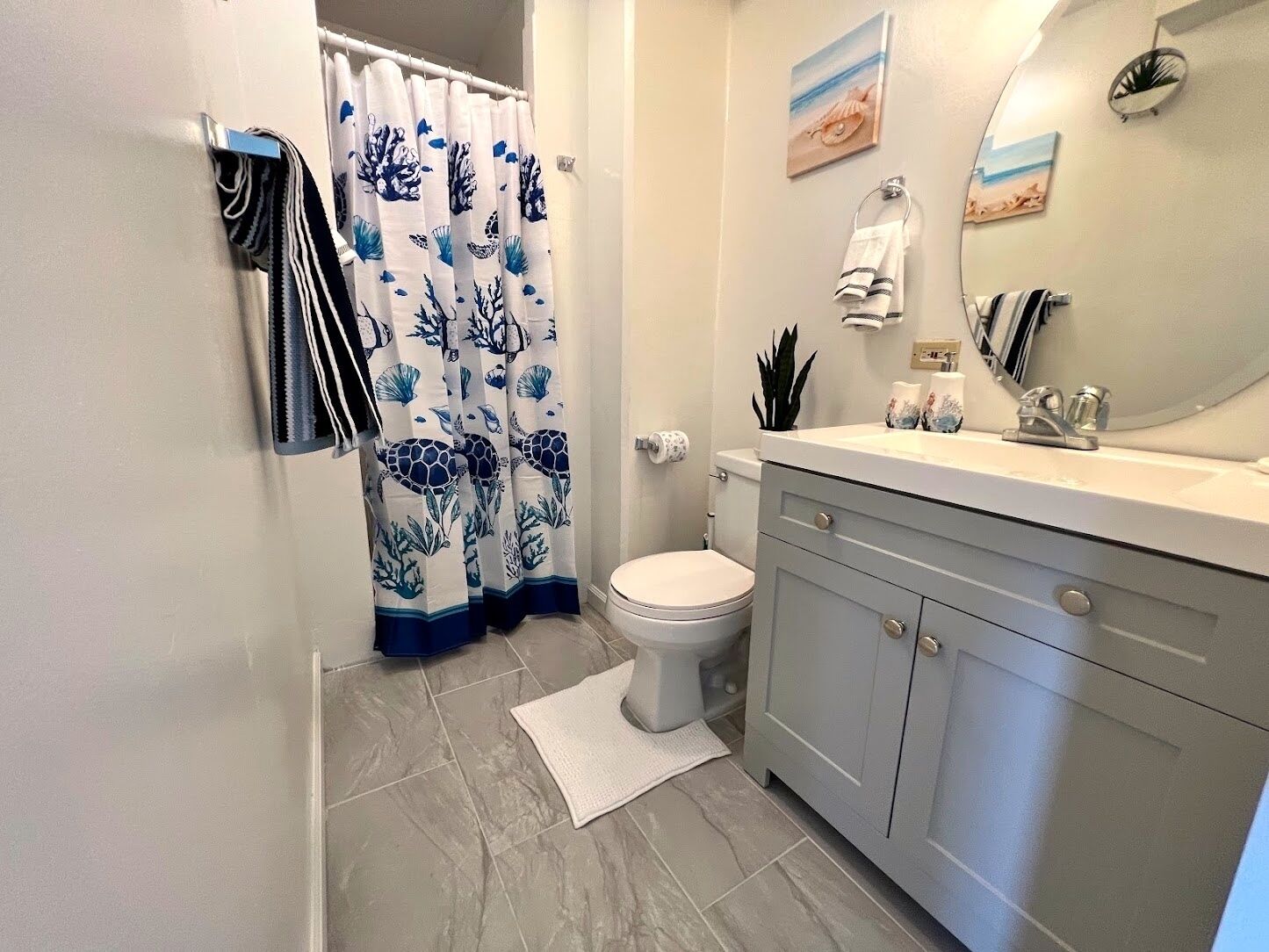 A bathroom with a toilet, sink, and shower curtain with a marine design.