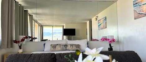 A bedroom with a bed, a TV, a window with curtains, and a painting on the wall.