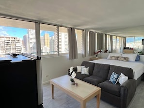 Una habitación de hotel moderna con una cama grande, un sofá, una mesita y un televisor.