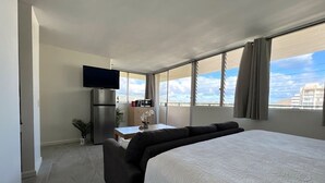 A hotel room with a large bed, a flat-screen TV, a kitchenette, and a view of the city. - Penthouse in Waikiki with ocean & mountain views 5 minutes walk to Waikiki beach (Honolulu)