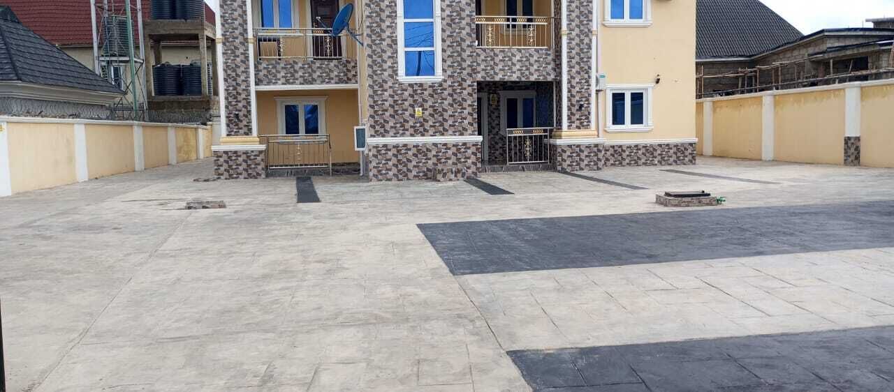 A multi-story residential building with a central entrance, balconies, and a paved courtyard.