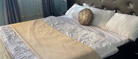 A neatly made bed with a tufted headboard, a beige throw blanket, and two pillows.