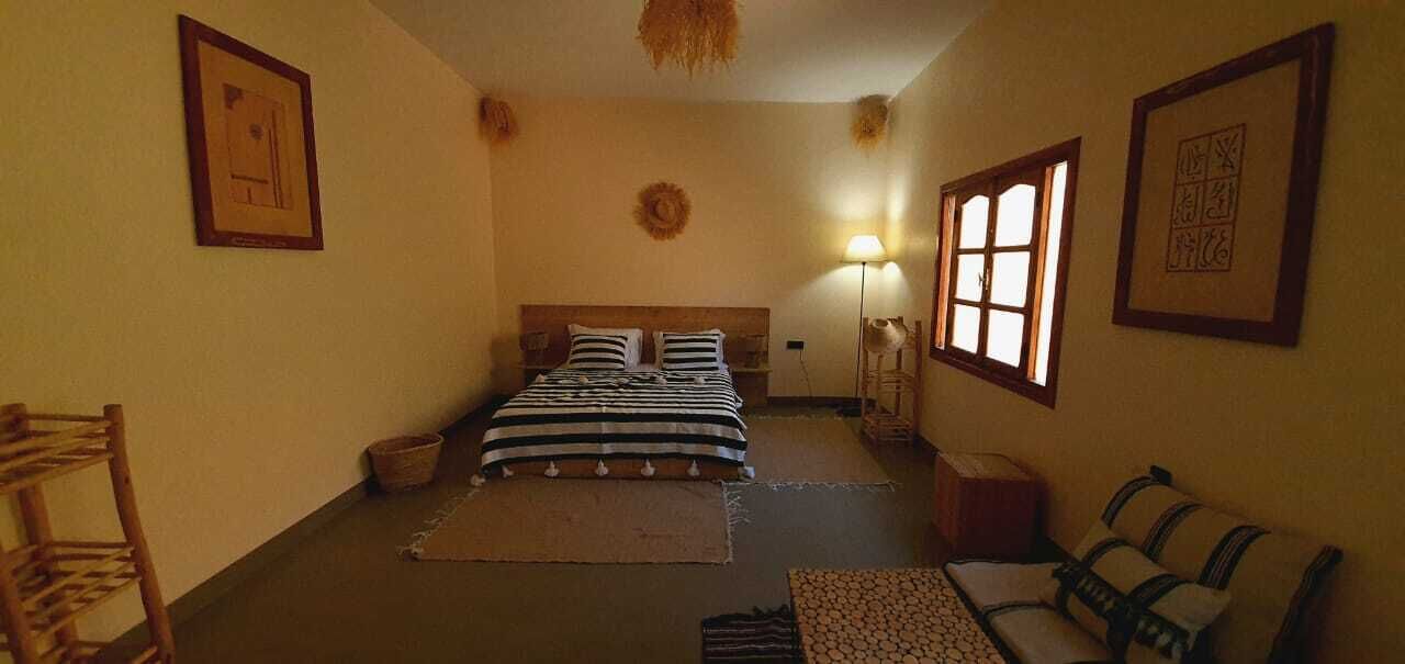 A bedroom with a bed, a nightstand, a lamp, a window, and a chair.
