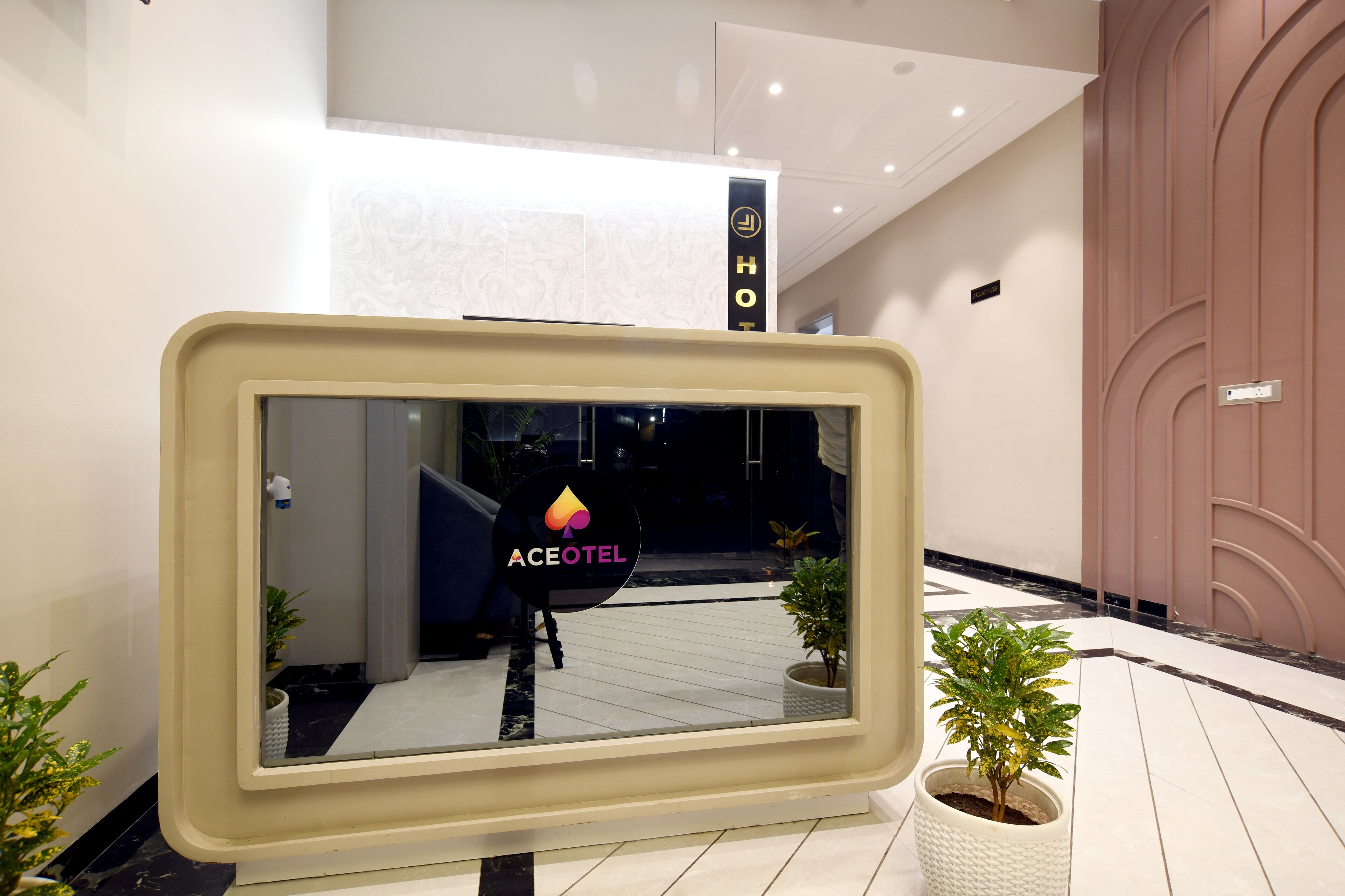 Un moderno vestíbulo de hotel con un espejo grande que refleja el interior, plantas en macetas y una escalera visible.