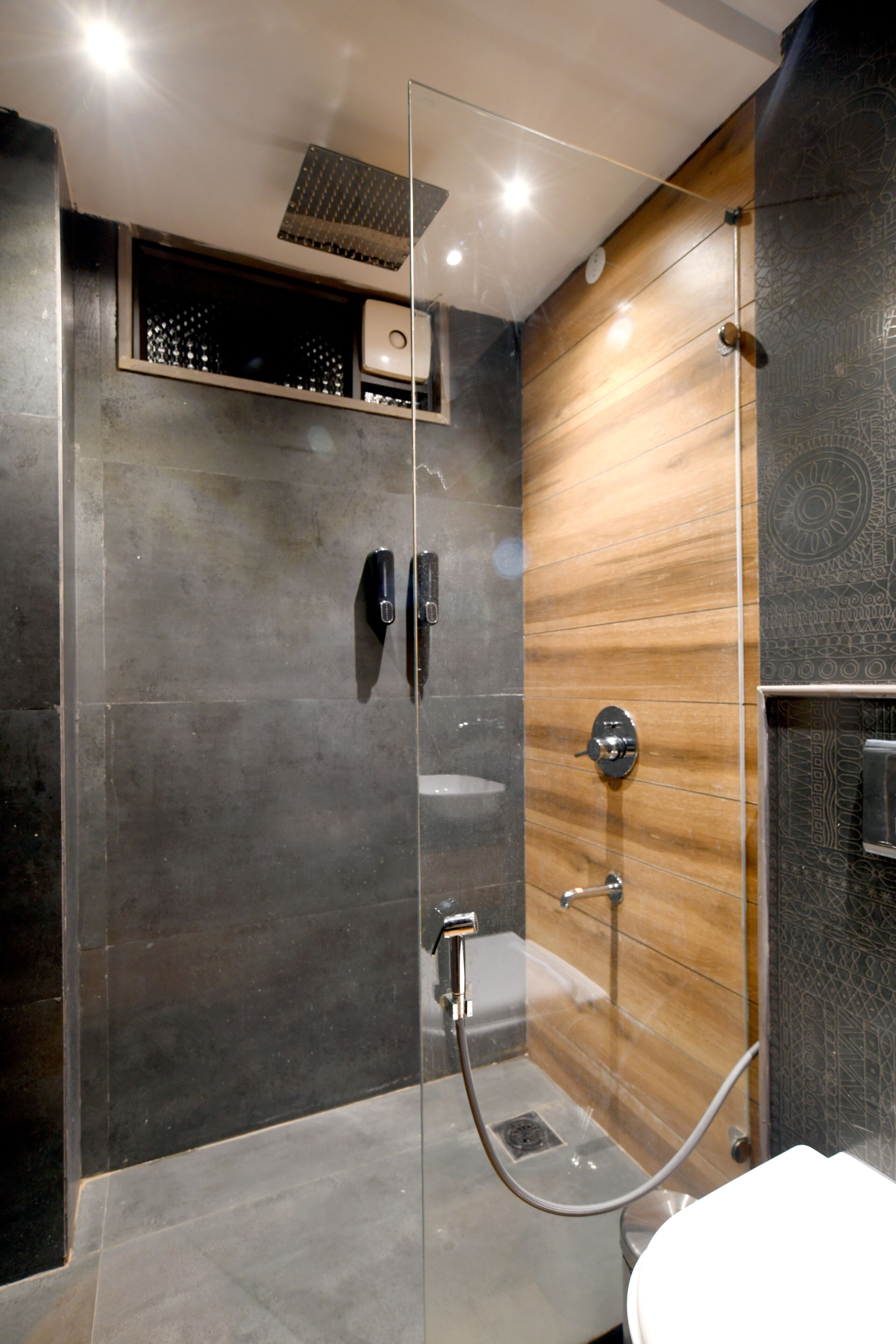Une salle de bain moderne dotée d’une douche à parois de verre, d’un mur d’accent en bois et d’un sol élégant recouvert de carreaux foncés.