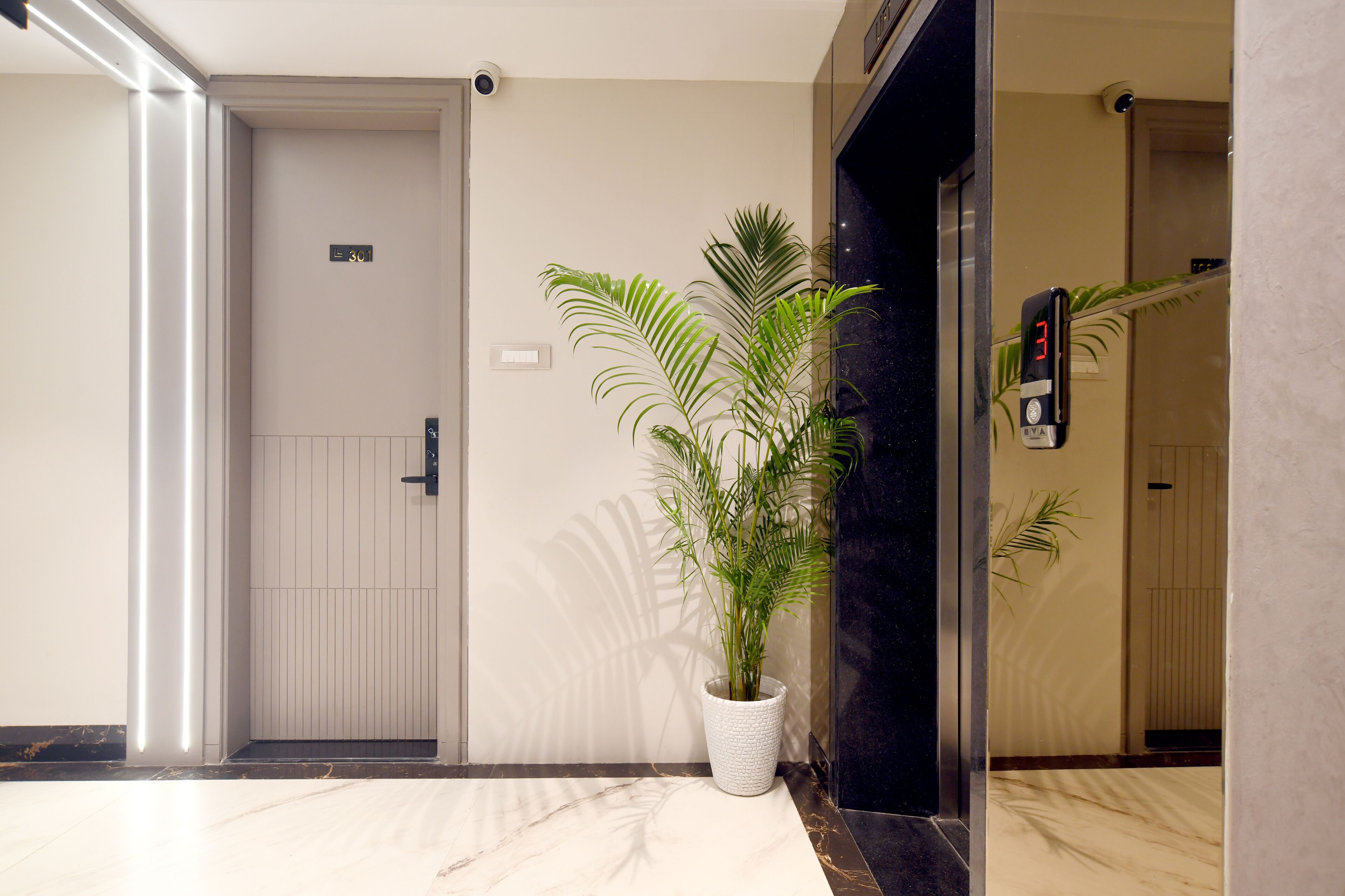 A modern elevator interior with a potted plant, a digital display, and a door with a number sign.