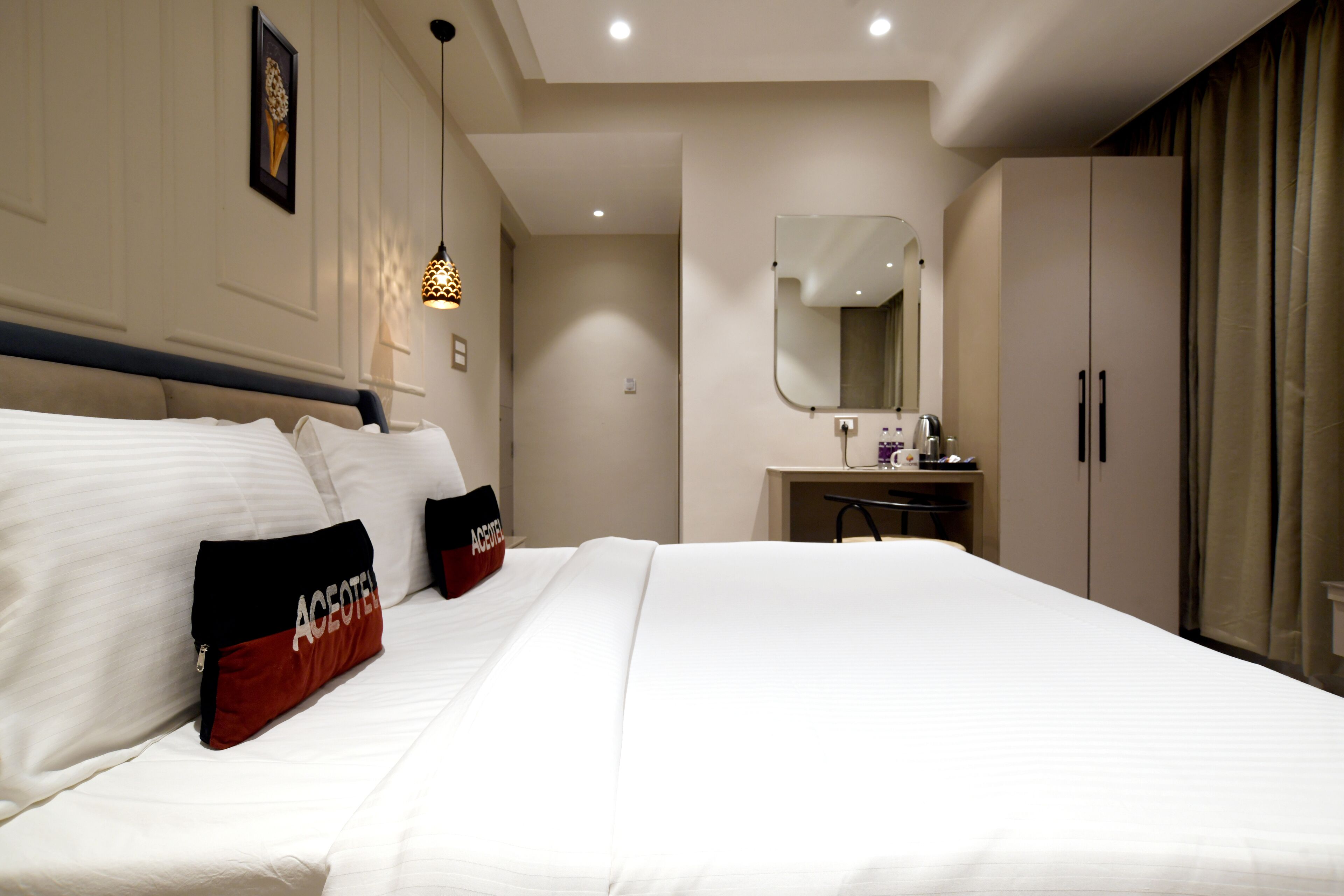 Hotellihuone, jossa on suuri sänky, työpöytä tuolilla, peili ja vaatekaappi.