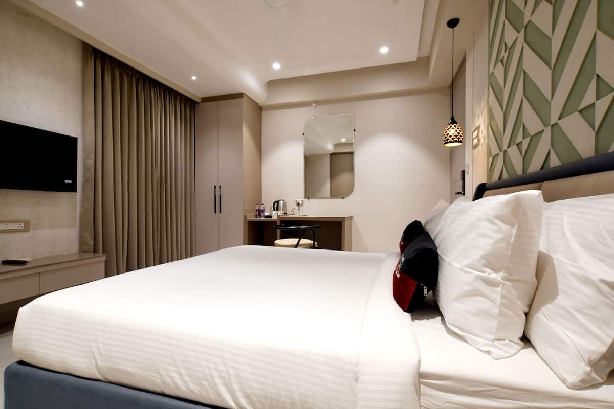 Una habitación de hotel moderna con una cama grande, una mesita de noche, un espejo y un televisor montado en la pared.