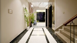 Um hall de hotel moderno com piso de mármore, escada e plantas em vasos.