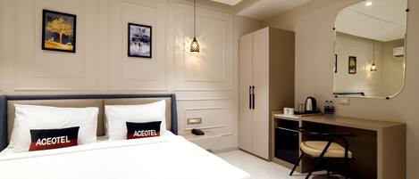 A modern hotel room with a bed, a desk, and a chair. There are framed pictures on the wall and a mirror above the desk.