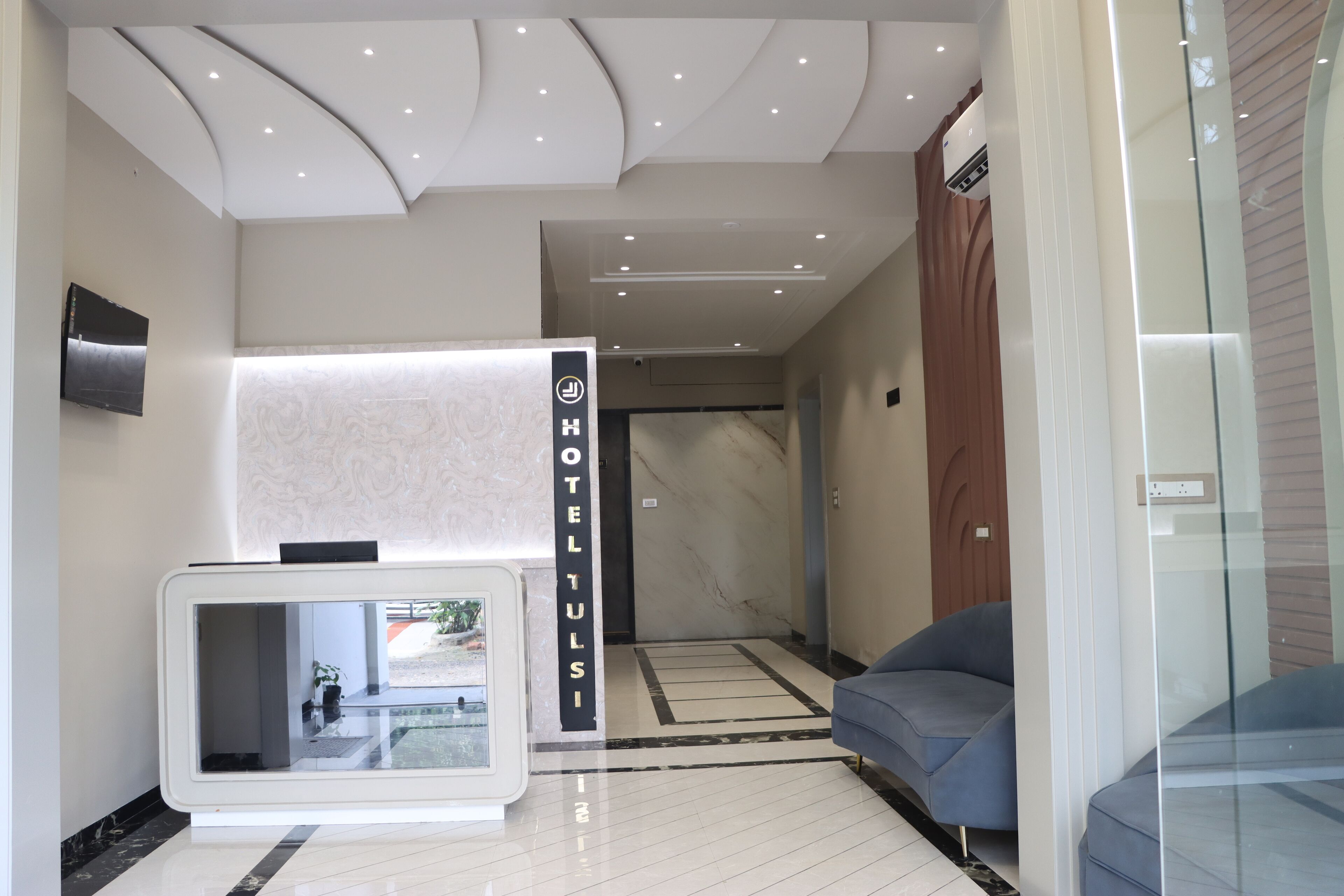Ein moderner Hotel-Empfangsbereich mit einer Rezeption, einem digitalen Bildschirm und einer blauen Lounge.