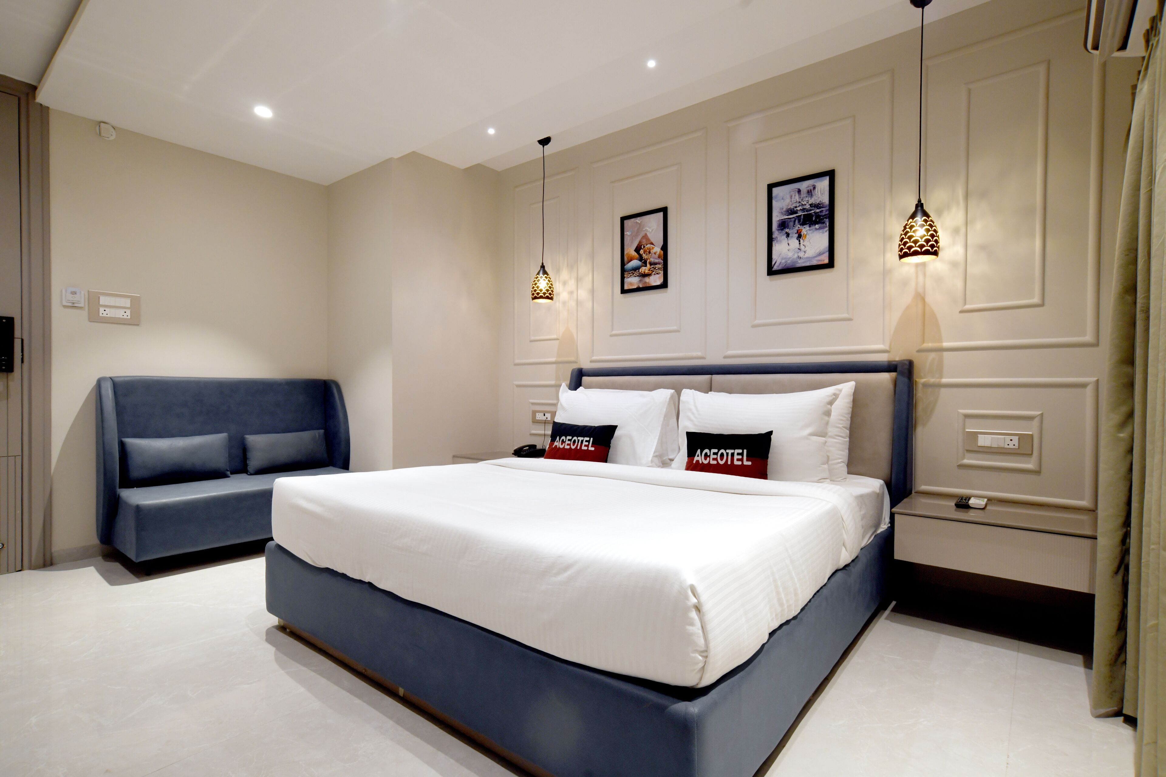 A modern hotel room with a large bed, a sofa, and two wall-mounted lights.