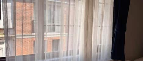 A room with a bed, a window with sheer curtains, and a radiator below the window.