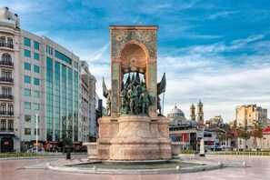 A public square with a central monument, surrounded by buildings.