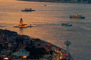 A waterfront cityscape with a prominent tower and a lit building, possibly a lighthouse, along with a busy waterway with boats. - Taksim Centre Geneva Hotel (Istanbul)