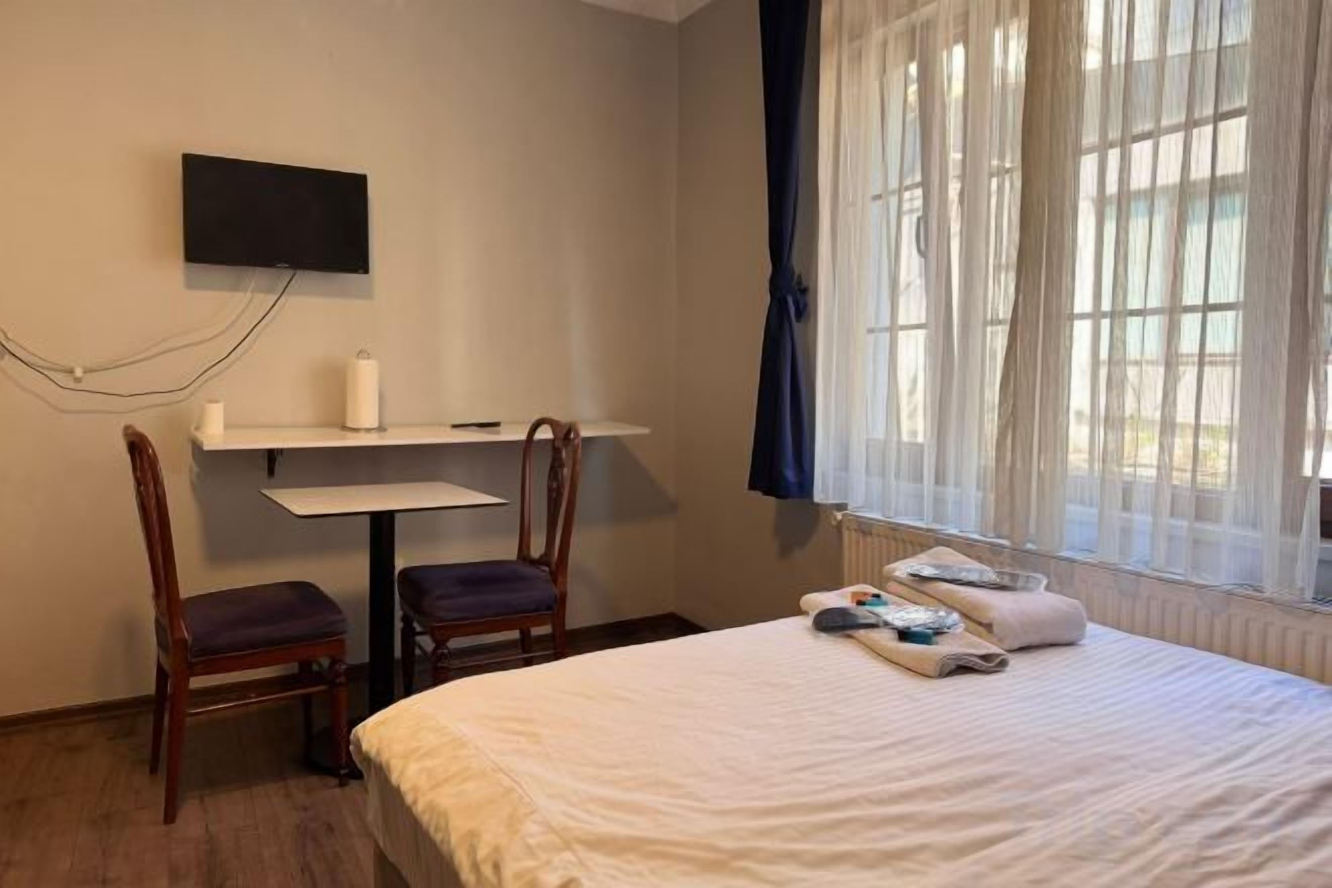 A hotel room with a bed, a desk, two chairs, a television, and a window with curtains.