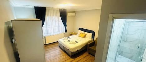 A compact hotel room with a bed, bedside table, and a refrigerator.
