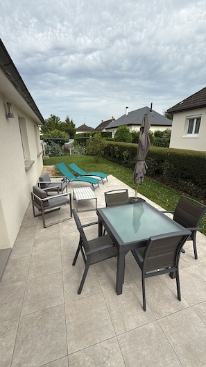 An outdoor patio with a glass-top table and chairs, surrounded by lounge chairs and a swimming pool.