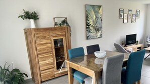 A dining area with a wooden table, blue and grey chairs, a glass cabinet with plants, and framed pictures on the wall. - Maison 4/6 Personnes - Bayeux et Plages du Débarquement (Bayeux)