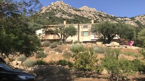 Un edificio de dos pisos con fachada de piedra, rodeado de árboles y una montaña al fondo.
