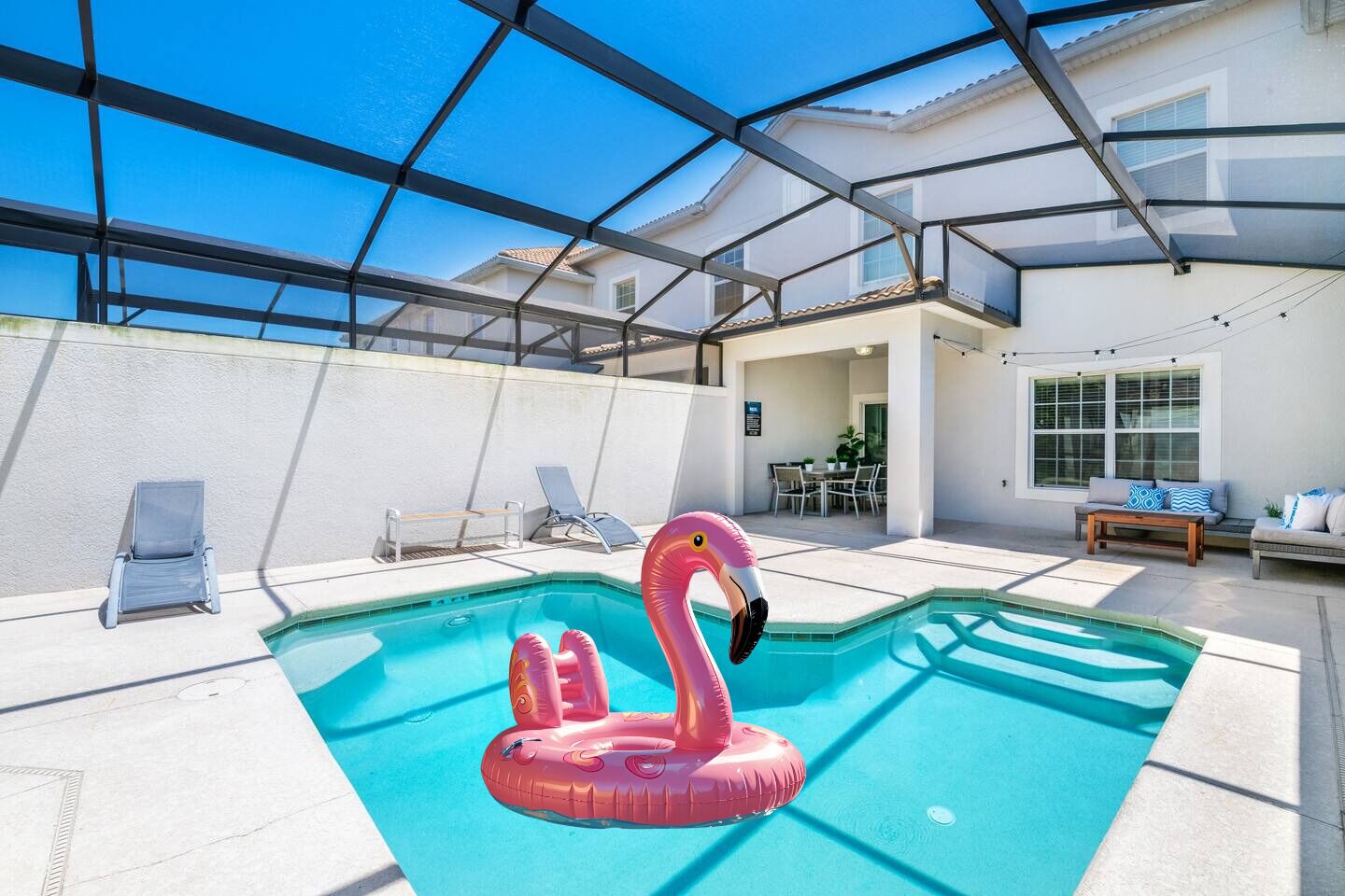 A swimming pool with a pink flamingo float, lounge chairs, and a covered patio area.