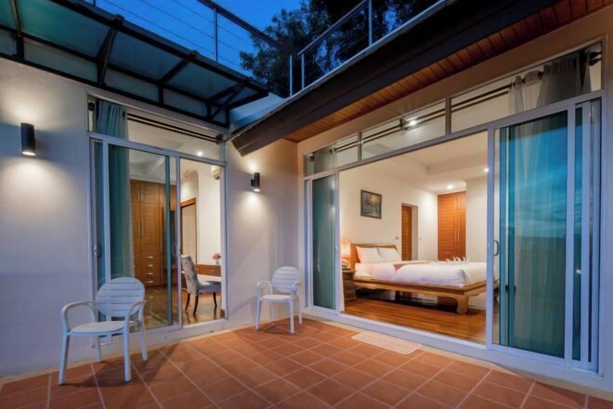 Une chambre moderne dotée d’un grand lit, de portes-fenêtres coulissantes et d’un petit coin salon avec des fauteuils.