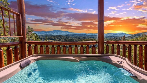 Uma banheira de hidromassagem com vista para as montanhas, deck de madeira e pôr do sol.