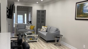 A modern living room with a grey sofa, a coffee table, and a dining area with chairs and a table. - Home with Park View on Yonge St Newmarket (Newmarket)