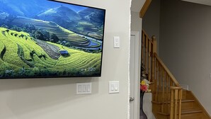 A flat-screen TV mounted on a wall, a wooden staircase, and a vase with flowers. - Home with Park View on Yonge St Newmarket (Newmarket)