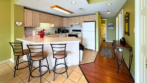 A kitchen with a central island, bar stools, wooden cabinets, a refrigerator, and a microwave.