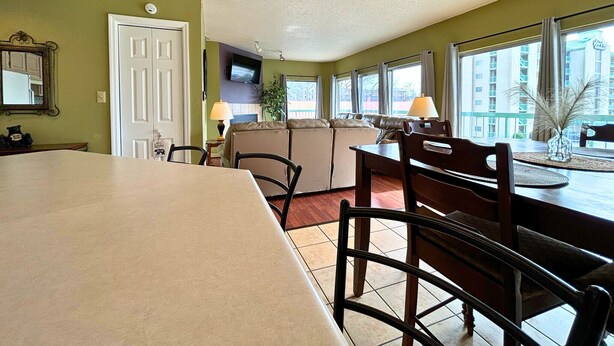 A dining area with a large table, chairs, a sofa, and a TV mounted on the wall.