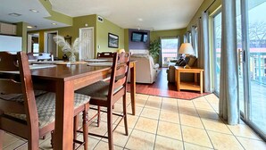 A spacious living area with a dining table, chairs, a sofa, and a TV mounted on the wall.