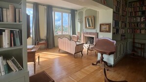 Ein geräumiger Raum mit Kamin, Bücherregalen, einem gestreiften Sofa und einem Esstisch.