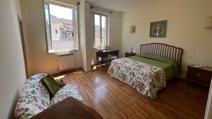 Ein Schlafzimmer mit Holzboden, einem Bett mit floralem Überwurf, einem grünen Sofa und einem Schreibtisch mit Stuhl.