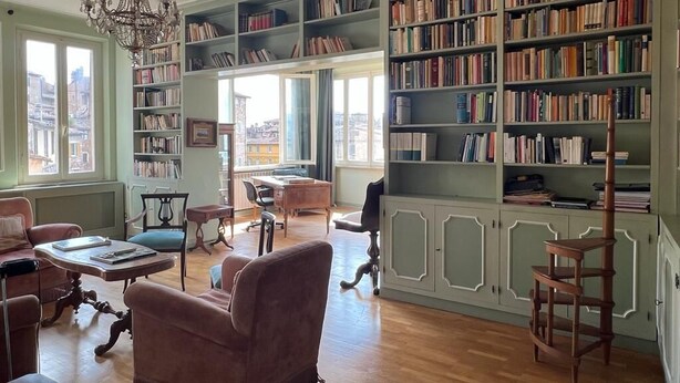 Eine großzügige Bibliothek mit mehreren Bücherregalen, bequemen Sitzmöglichkeiten und einem großen Fenster mit Blick.
