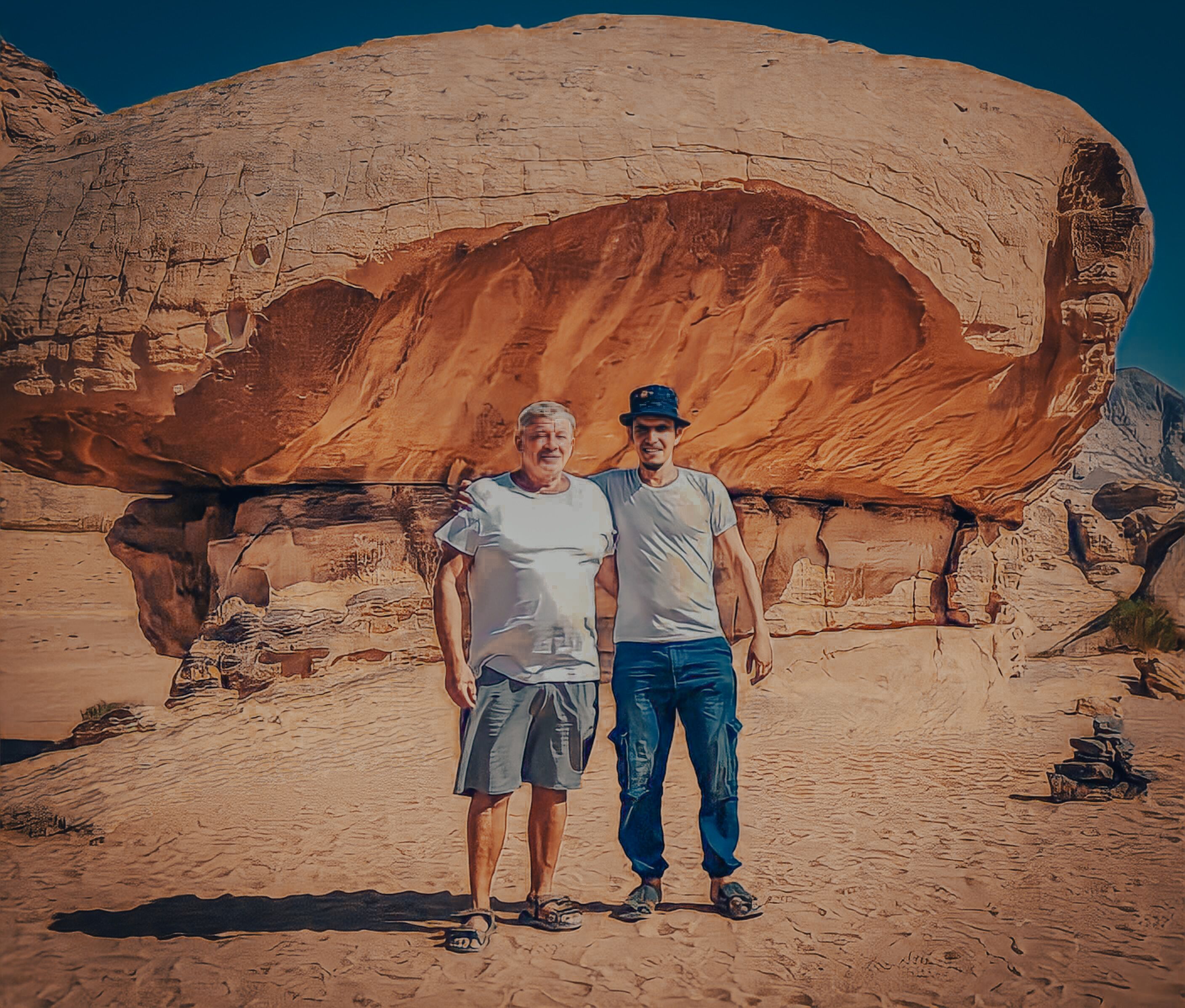 Two people standing in front of a large rock formation.