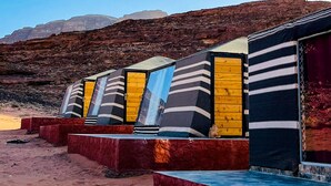A row of colorful, striped beach huts with a rocky desert background. - Miral Night Camp (Wadi Rum)