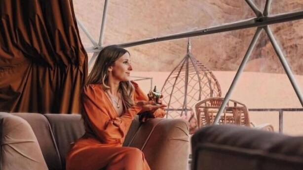 A person sitting on a sofa inside a tent-like structure with a view of a desert landscape. - Miral Night Camp (Wadi Rum)