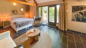 A bedroom with a bed, bedside tables, a chair, a small table, and a large window with curtains.