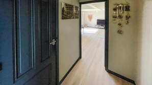 A hallway with a wooden floor, a dark door, and a wall with a framed picture and a wall-mounted display of shells.