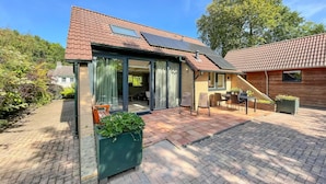 A modern house with a tiled roof, large windows, and a patio area with outdoor furniture.