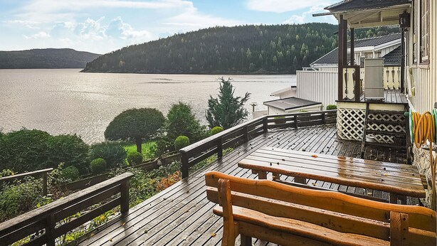 Un molo di legno con una panchina che si affaccia su un lago, circondato dal verde e da un edificio con tetto in tegole.