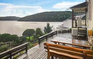 Une terrasse en bois avec un banc donnant sur un lac, entourée de verdure et bordée d’un bâtiment dont le toit est recouvert de tuiles.