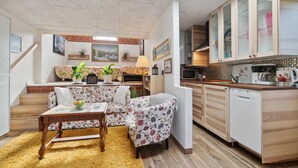 A compact living space with a sofa, a dining table, a kitchen area with cabinets and appliances, and a staircase leading to an upper level.