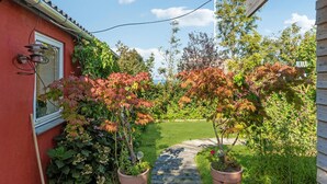 A garden pathway leading to a house with a red exterior, potted plants, and a clear sky.